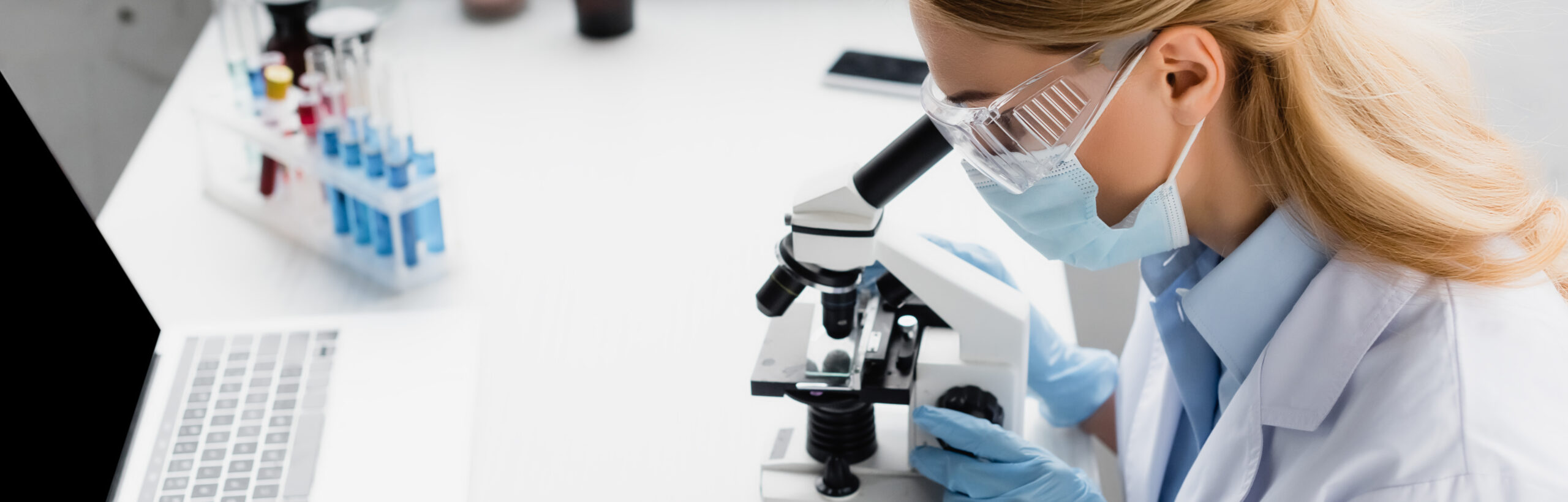 Masked worker in lab with microscope and computer