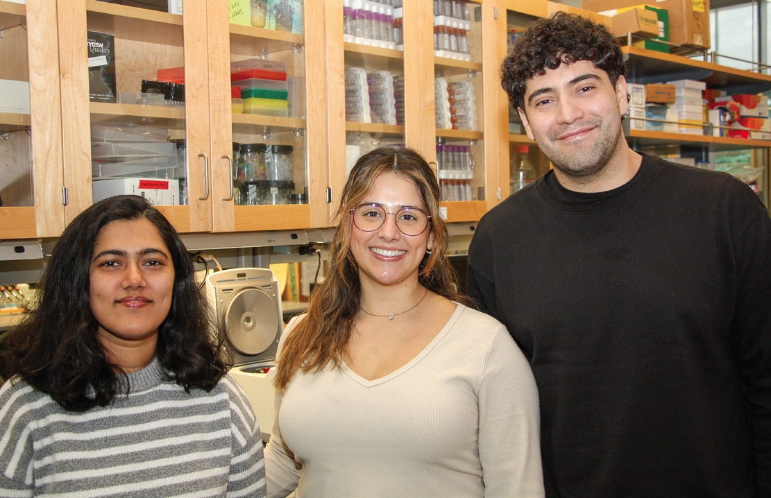 Three students pose for photo in the lab with lab equipment in the background