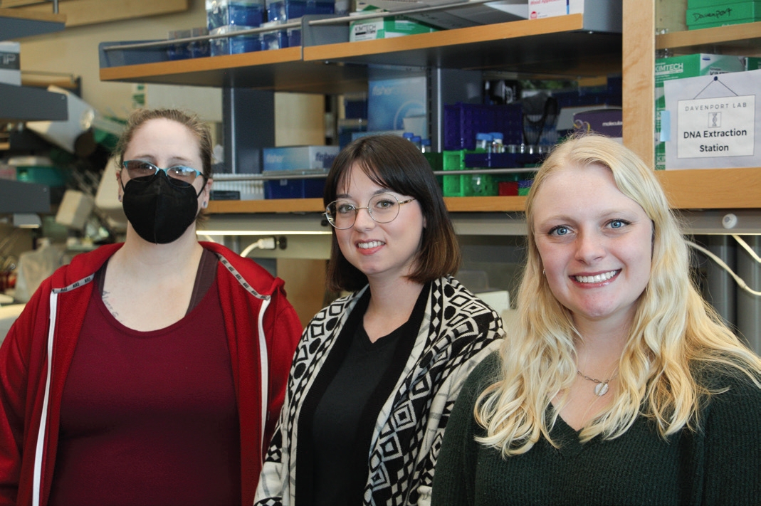 Three students posing for photo in the lab with lab equipment in the background