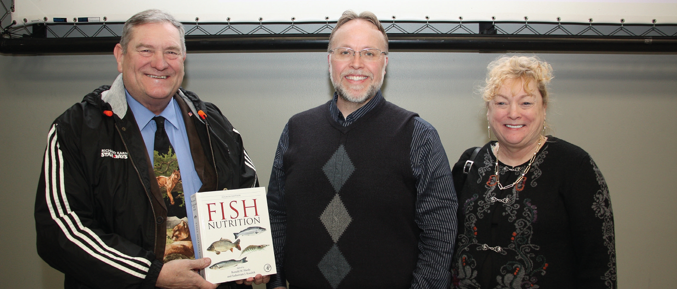 Peter and Deborah Halver pose for a photo with Matt Brooks. Peter is holding a copy of "Fish Nutrition".