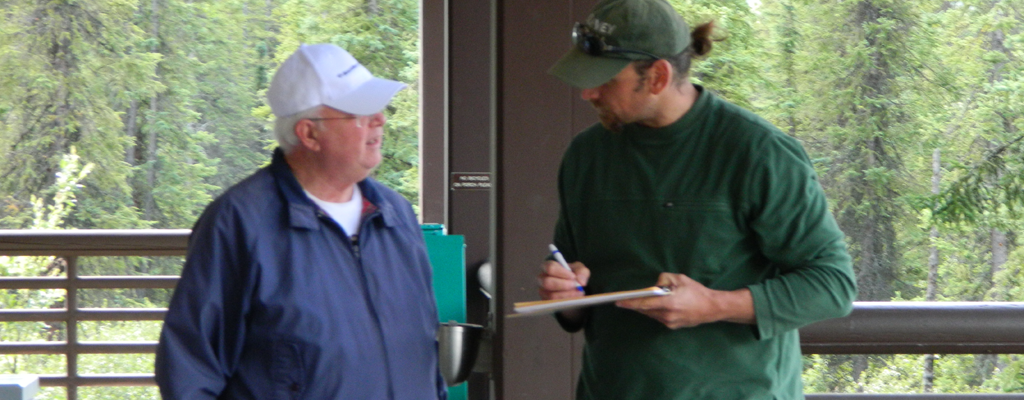 Two people talk with one person having a clipboard.