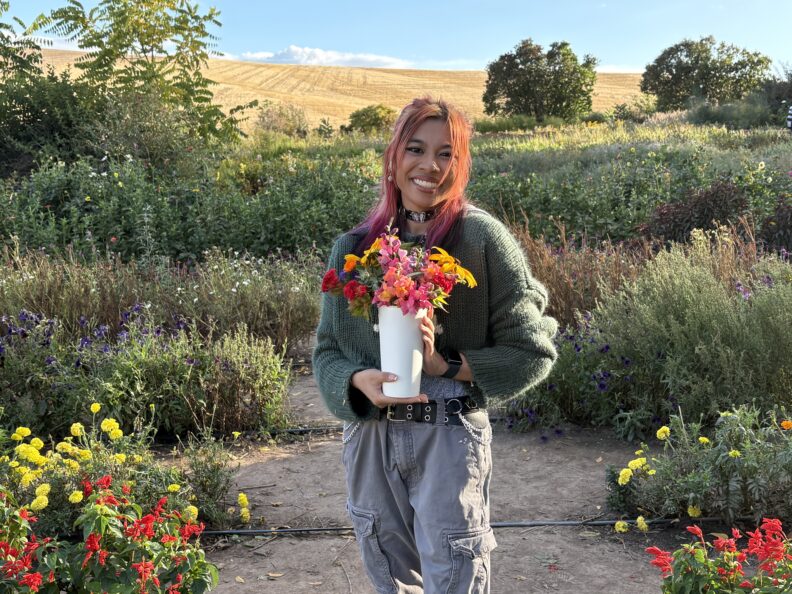 OL Emi holds a vase of bright flowers in a garden