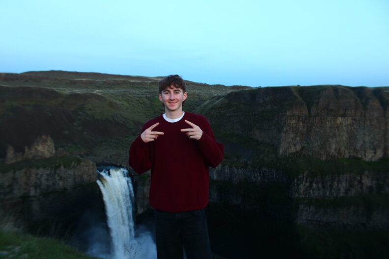 OL Andrew smiles and makes peace signs in front of a waterfall