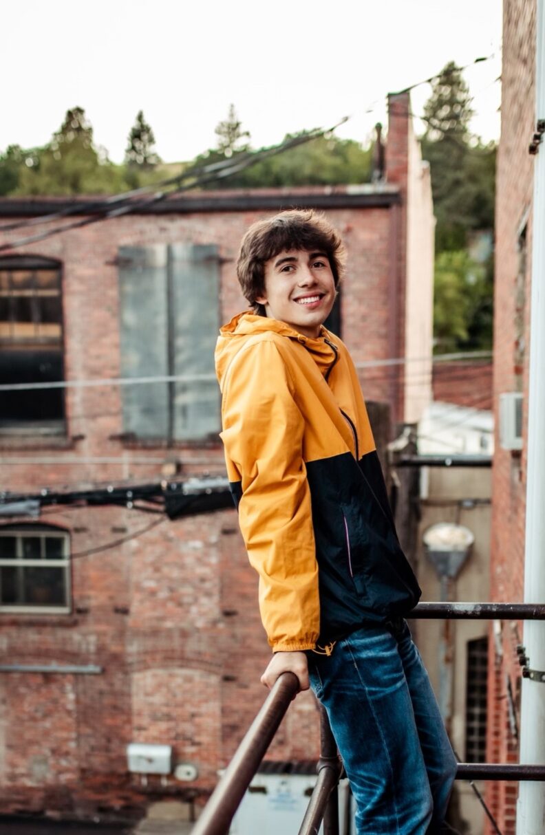OL Bradyn smiles on a balcony outside a brick buildning