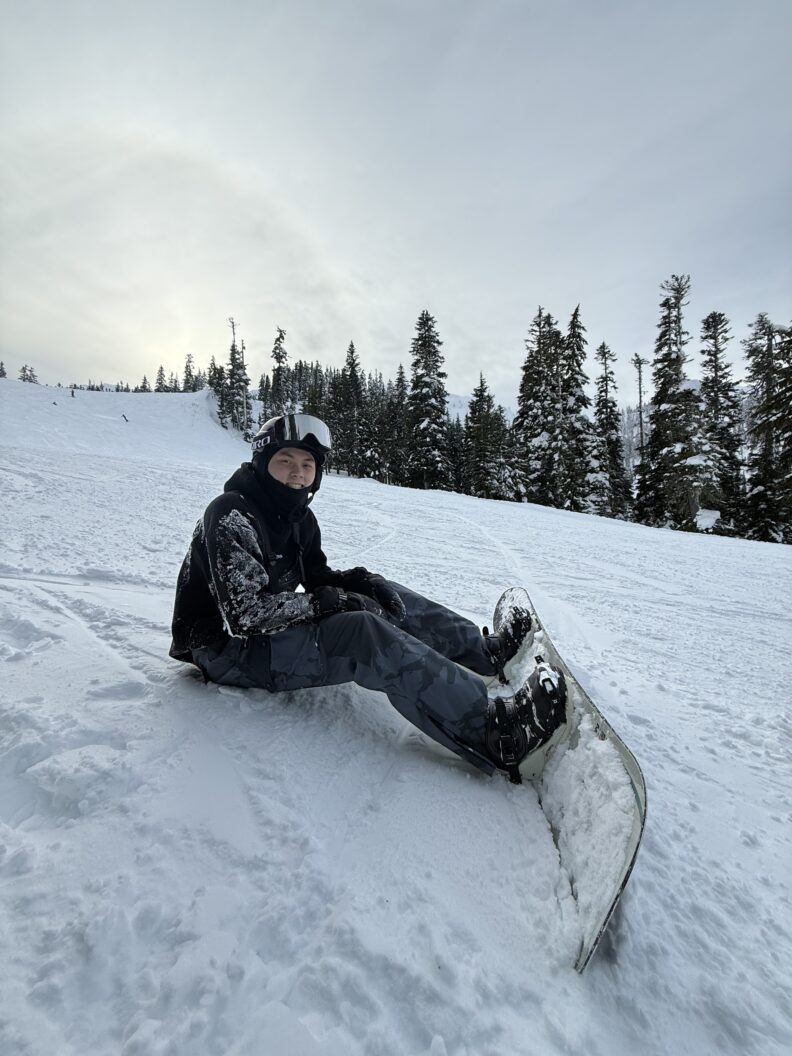 OL Ethan sits on the side of a snowy mountain while snowboarding.