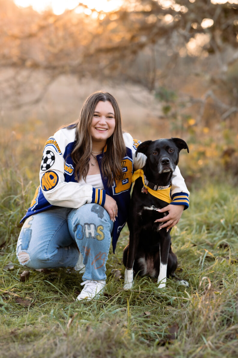 OL Lexi wears a letterman jacket and has her arm around her dog wearing a matching scarf.