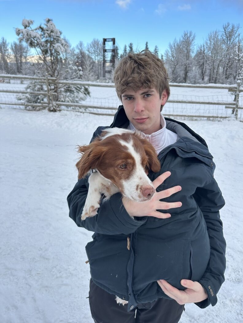 OL Payton standing in the snow and holding his dog inside of his blue winter jacket.