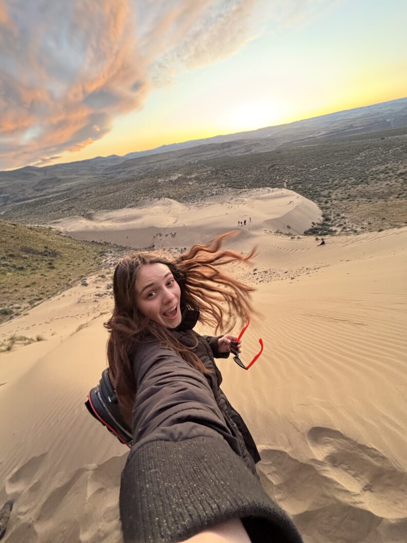 Selfie of OL Zoe standing on top of a sand dune with hair blowing in the wind.