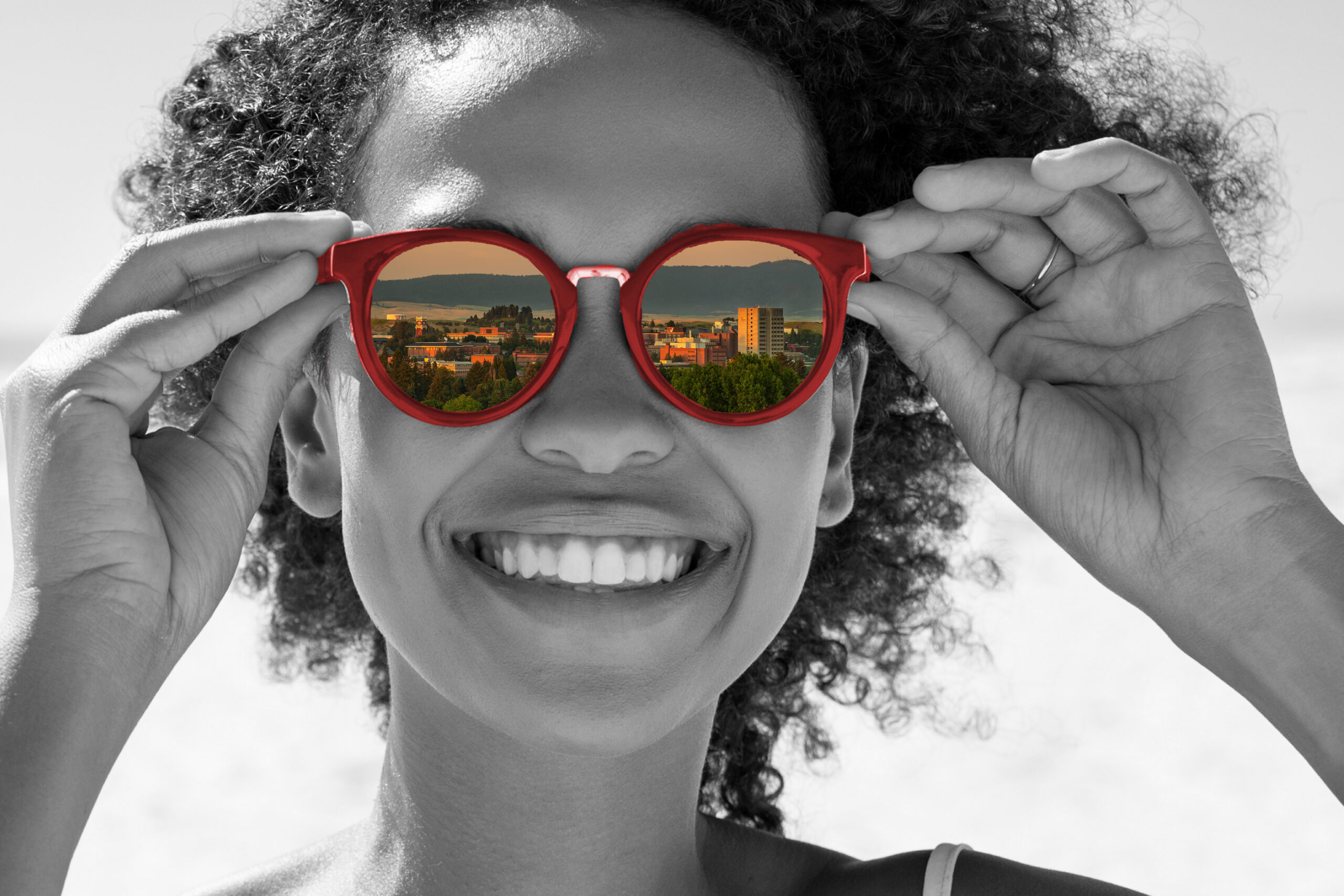 A woman holding glasses with WSU in the reflection