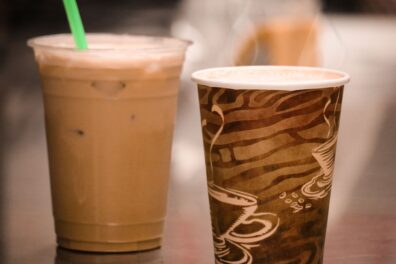 Coffee drink in a plastic cup next to a drink in a paper cup