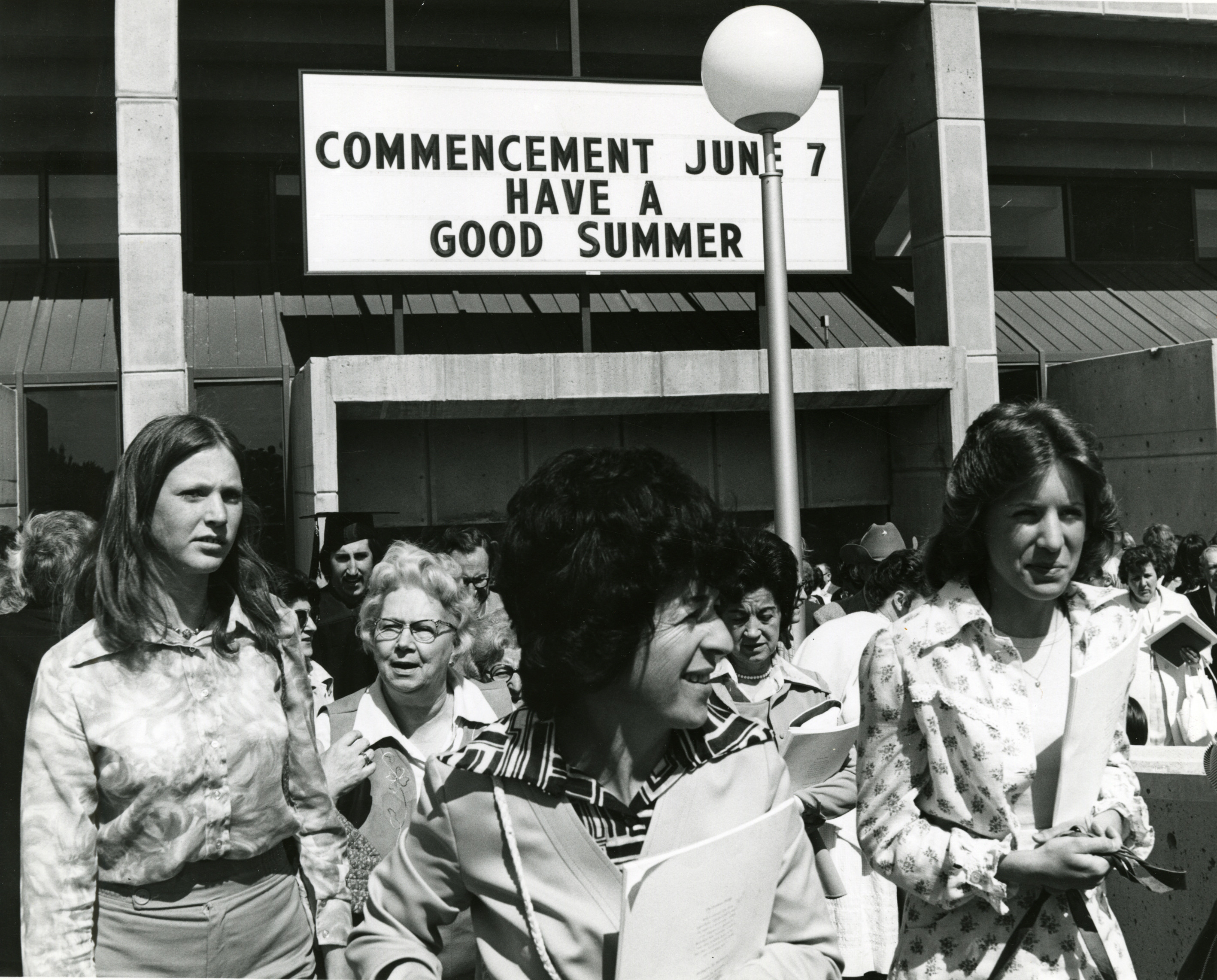 Early 1970's era black and white photo of a people exiting Beasley, in the background is s sign reading Commencement June 7, Have a good summer".