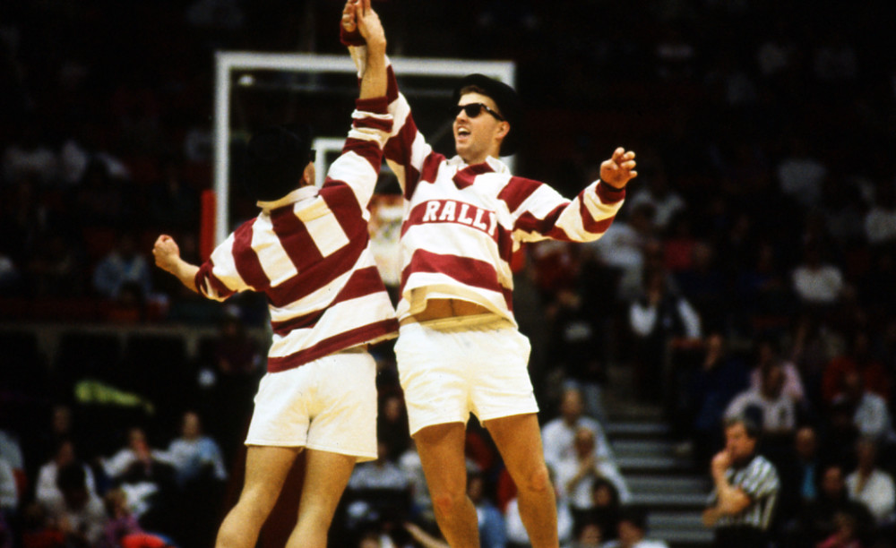 Two student in bold crimson striped shirts jumping in the air to celebrate.