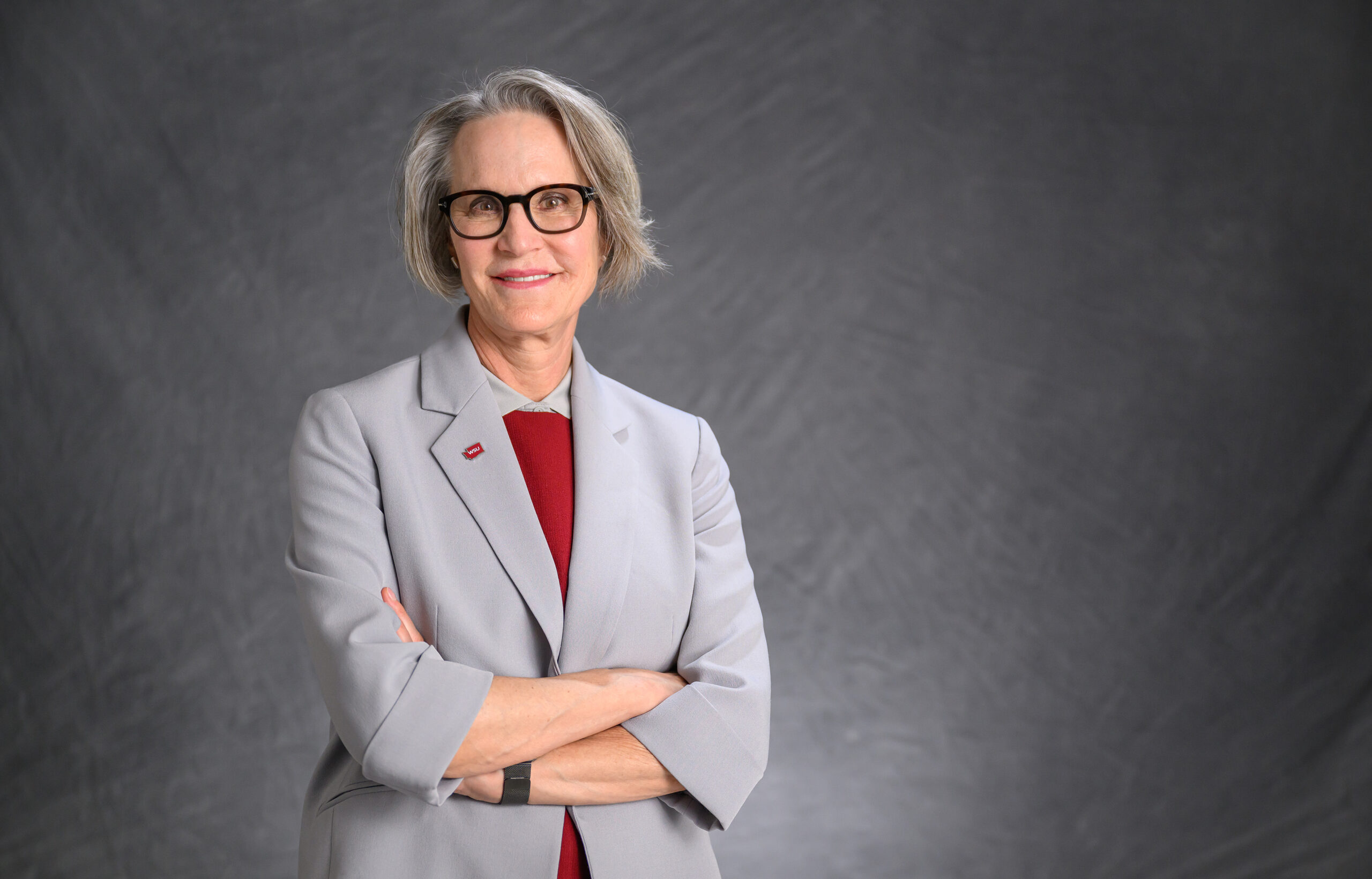 A close-up of the WSU president, wearing a grey jacket and red shirt, smiling at the camera. 
