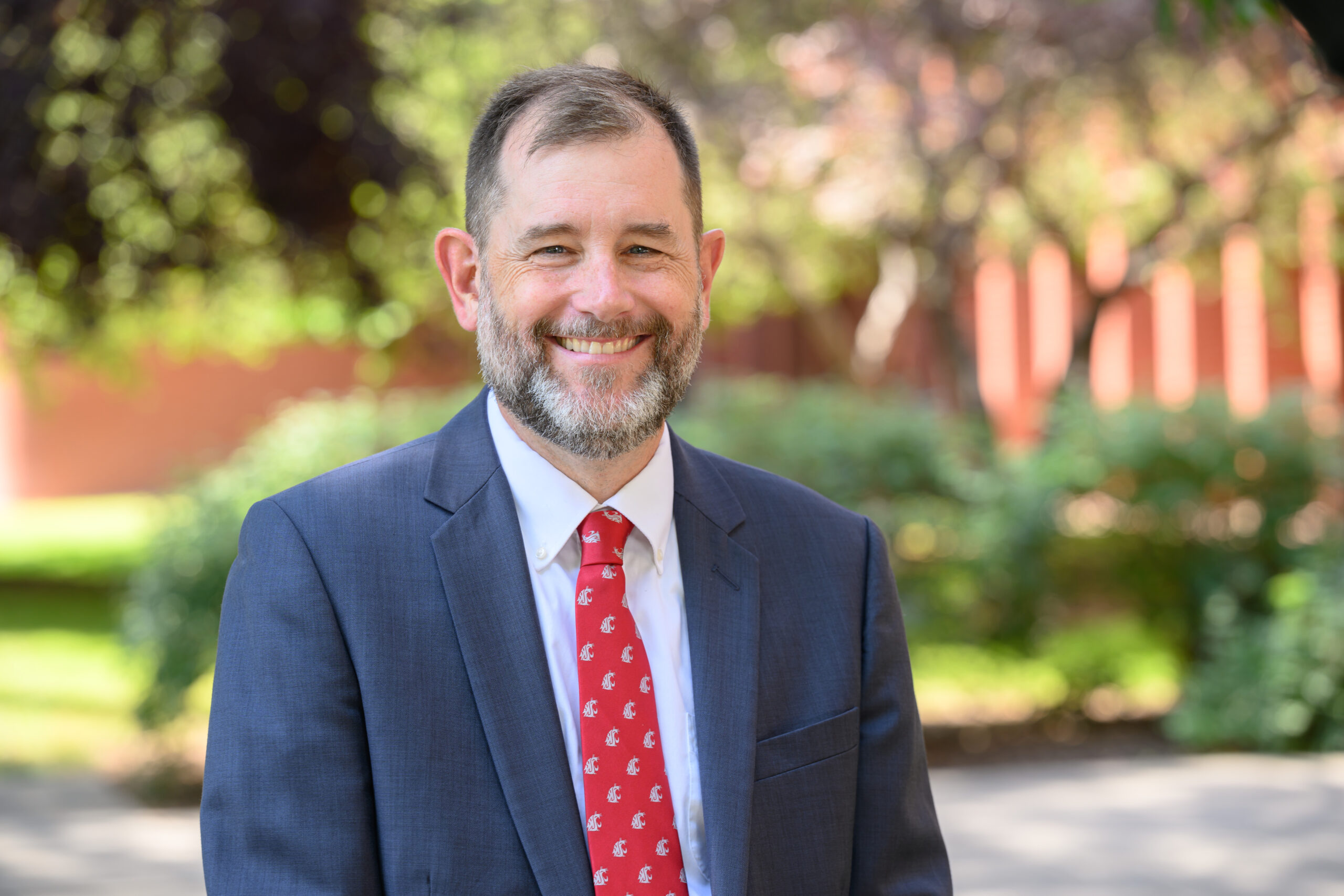A close up of the WSU provost, wearing a blue jacket and red tie, smiling at the camera. 