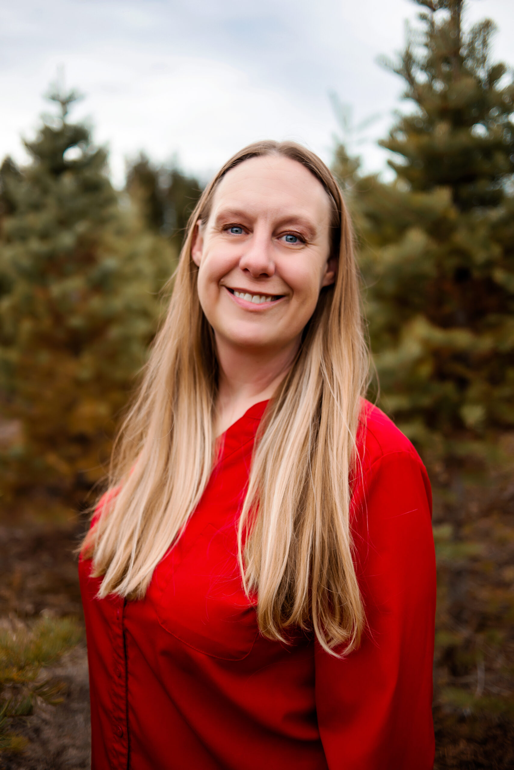 A university faculty member standing in front of pine trees, smiling at the camera. 