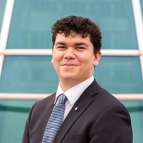 A close-up of a student dressed in a suit & tie, in front of a blue background. 