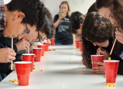 View down a table of students playing a team building activity involving straws, candy corn, and plastic cups at the 2022 Fall Social.