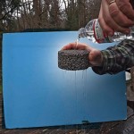 Person pouring water over a piece of pervious pavement and demonstrating that the water flows through.
