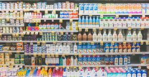 Fully stocked grocery store dairy aisle with rows of milk, creamers, and other refrigerated products.