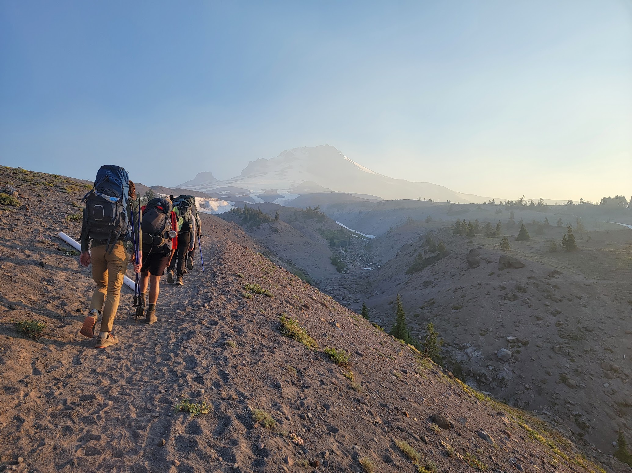 Students wearing hiking packs travel across the high desert towards a distant mountain rainge.