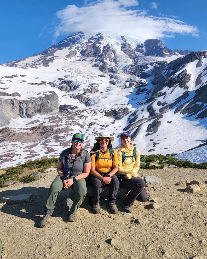 Three environment students sit at the base of a snow covered mountain.