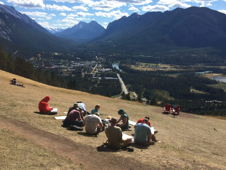 Students sitting outside near a mountain range.