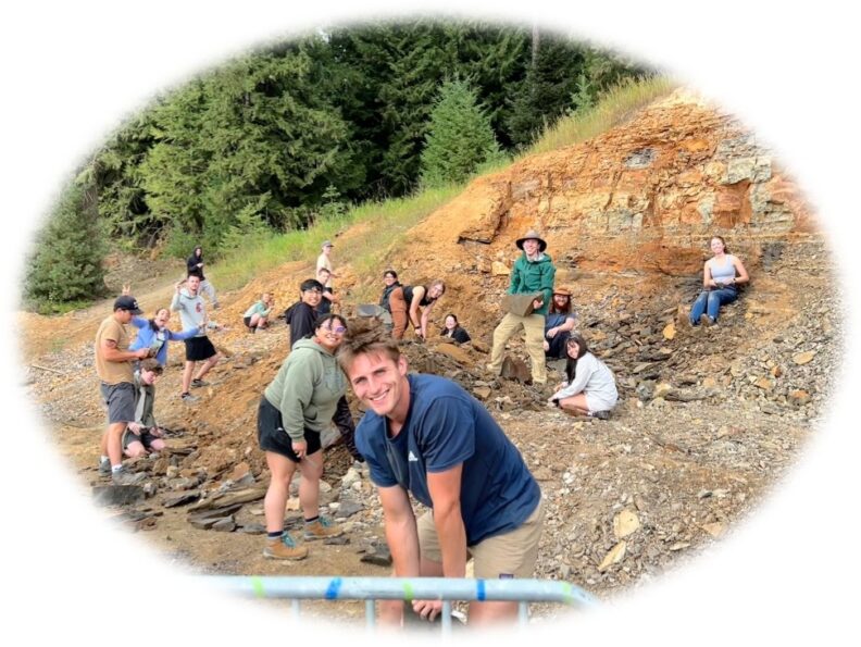 A group of SoE geology students posing for a photo among rocks and a rocky cliff.