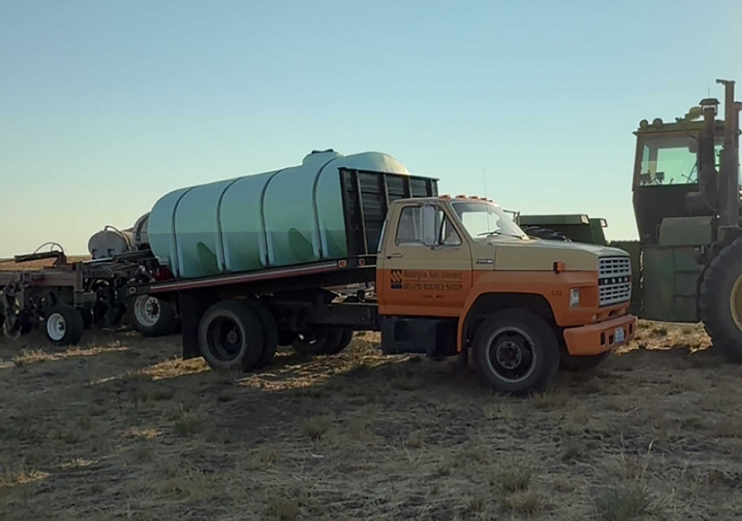 Water truck next to a tractor and drill.