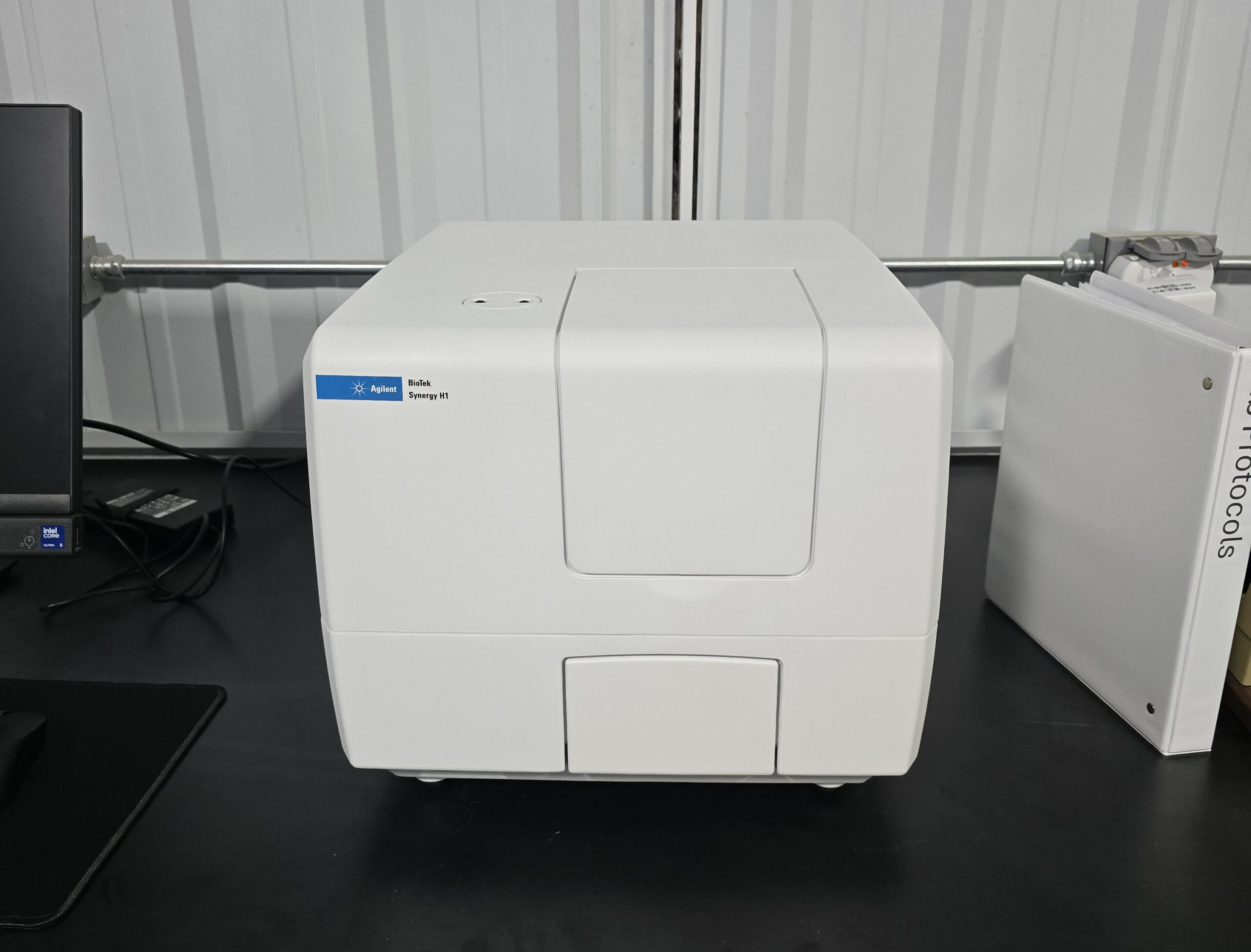 Plate reader next to a computer and a binder.