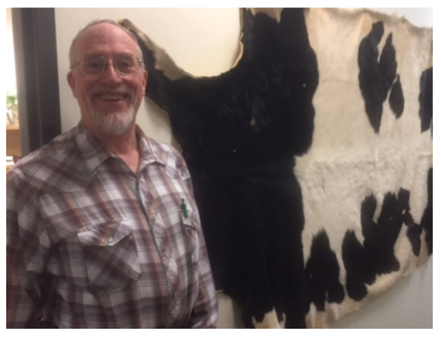 Dr. Tom Brignole standing in front of a cow hide hanging on the wall.