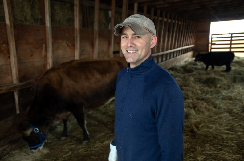 Craig McConnel in a barn with two cows behind him.