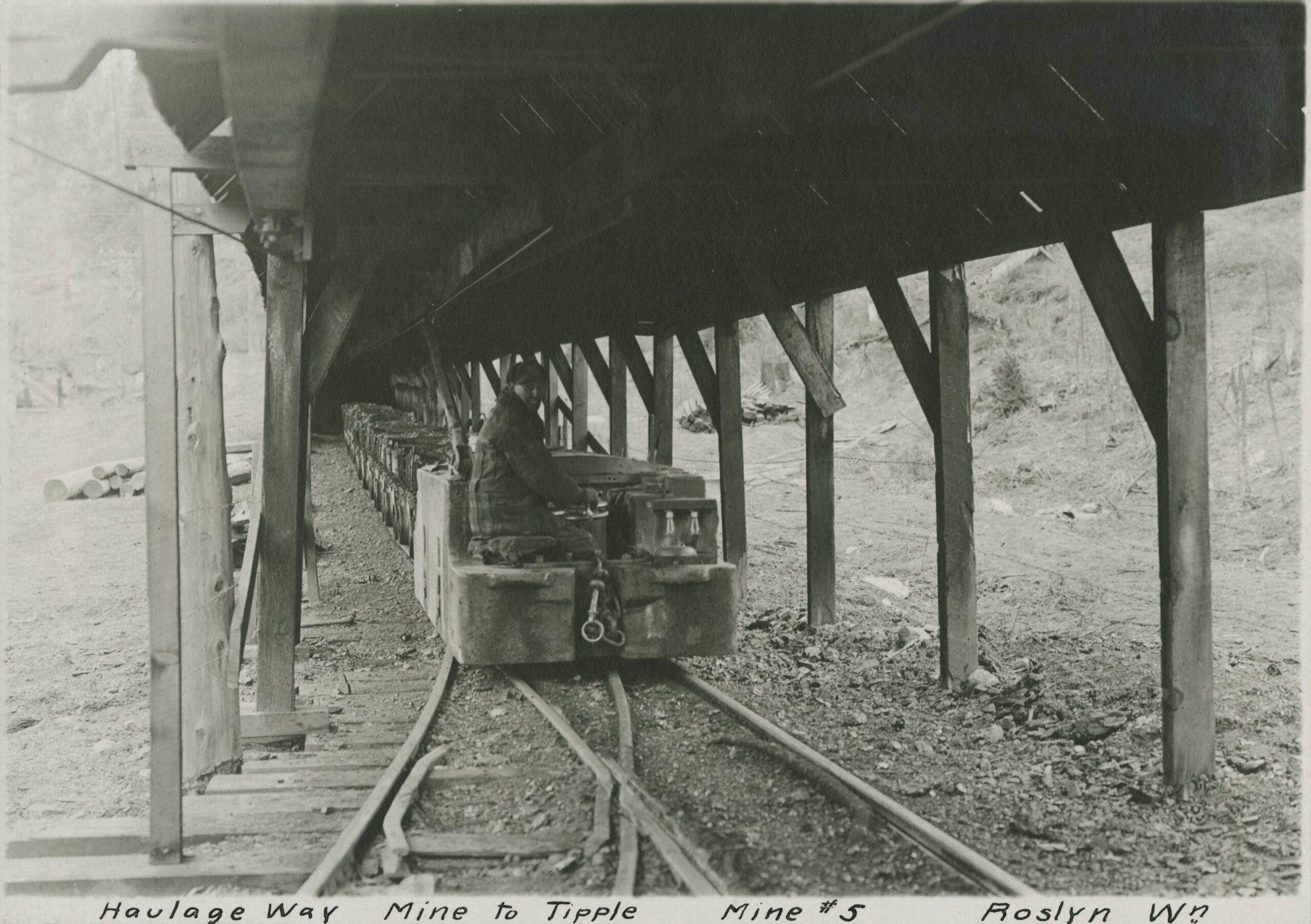 Photo of a man in a mining car on tracks under a wooden structure