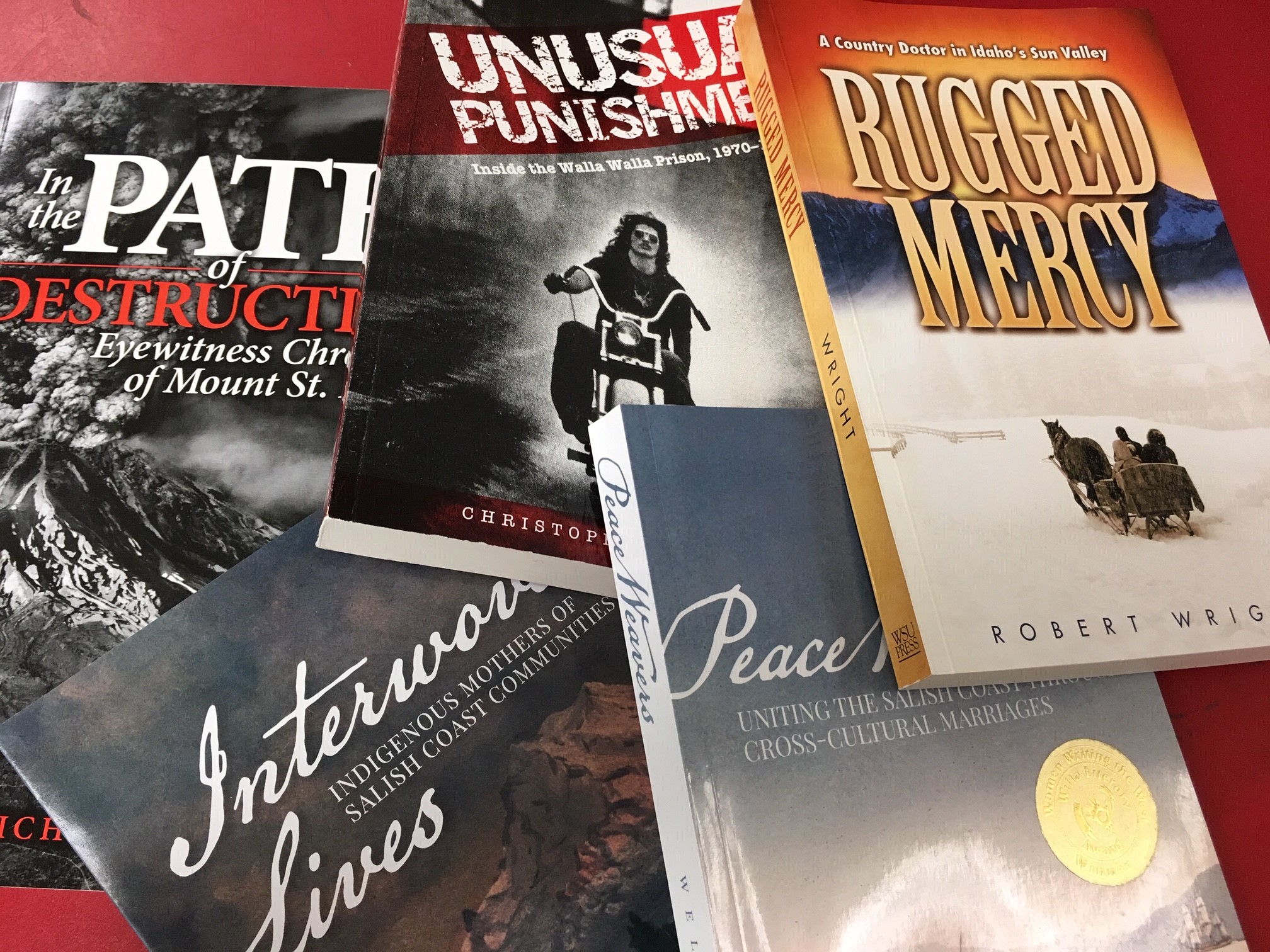 Image of five books on a table: In the Path of Destruction, Interwoven Lives, Peace Weavers, Rugged Mercy, and Unusual Punishment