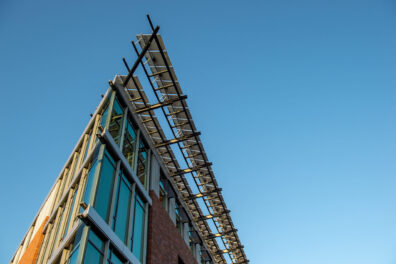 The top corner of a building emphasizing the extreme point of view and triangular shape of the top corner with the blue sky in the background.