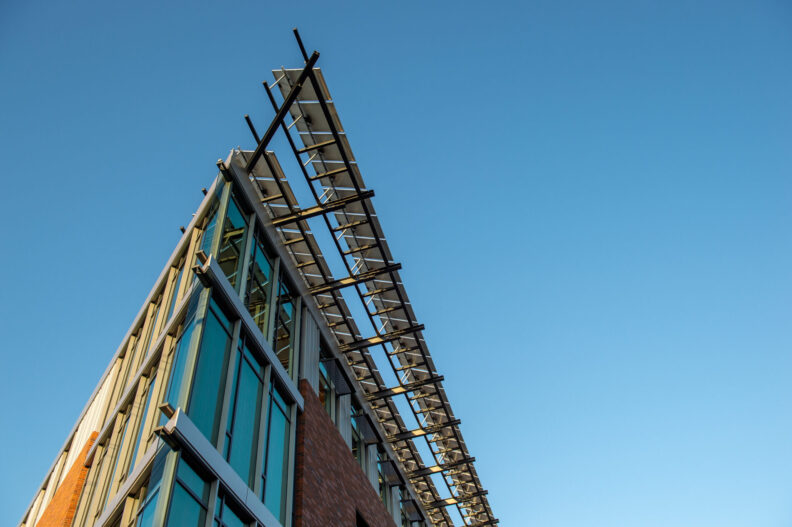 The top corner of a building emphasizing the extreme point of view and triangular shape of the top corner with the blue sky in the background.
